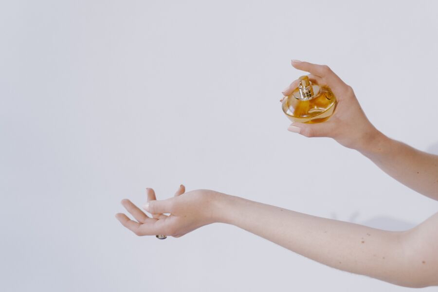 Primer plano de manos elegantes rociando perfume, mostrando belleza y lujo sobre un fondo blanco.