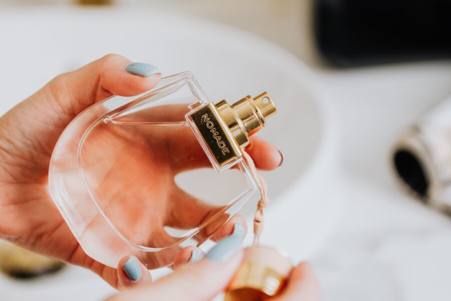 Primer plano de una mano cuidada que sostiene un frasco de perfume transparente con una tapa dorada, enfatizando la elegancia y la fragancia.