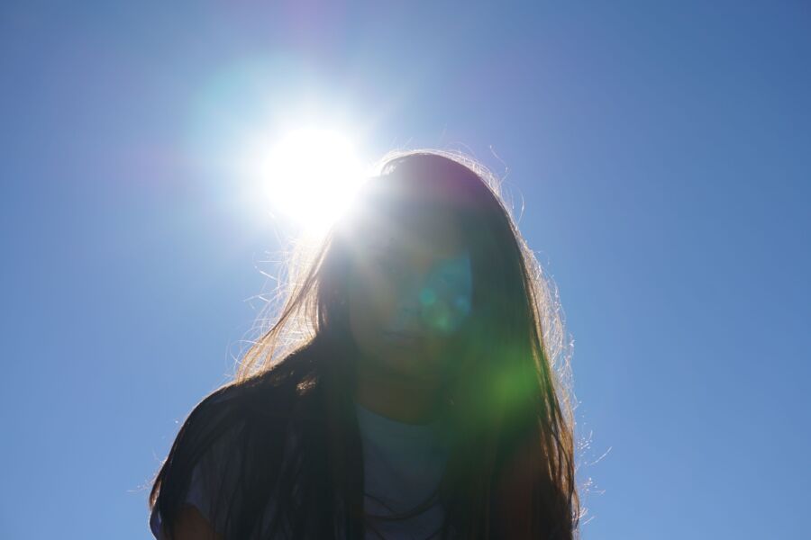 Retrato retroiluminado de una mujer con destellos de sol contra un cielo azul brillante.