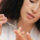 Primer plano de una mujer joven aplicando suero para el cuidado de la piel con una pipeta sobre un fondo rosa.