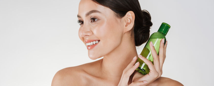Retrato de belleza de mujer morena sonriente con piel suave y saludable con loción para quitar el maquillaje, aislado en blanco