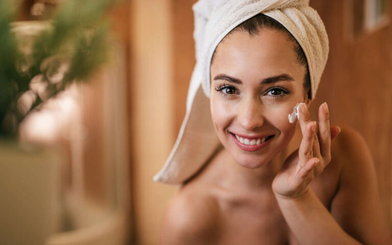 Mujer hermosa aplicando crema hidratante en su cara en el baño