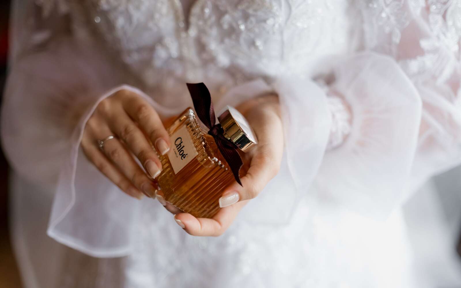 Una novia en vestido de encaje blanco con una botella de perfume Chloe de lujo, que simboliza la elegancia y el estilo.