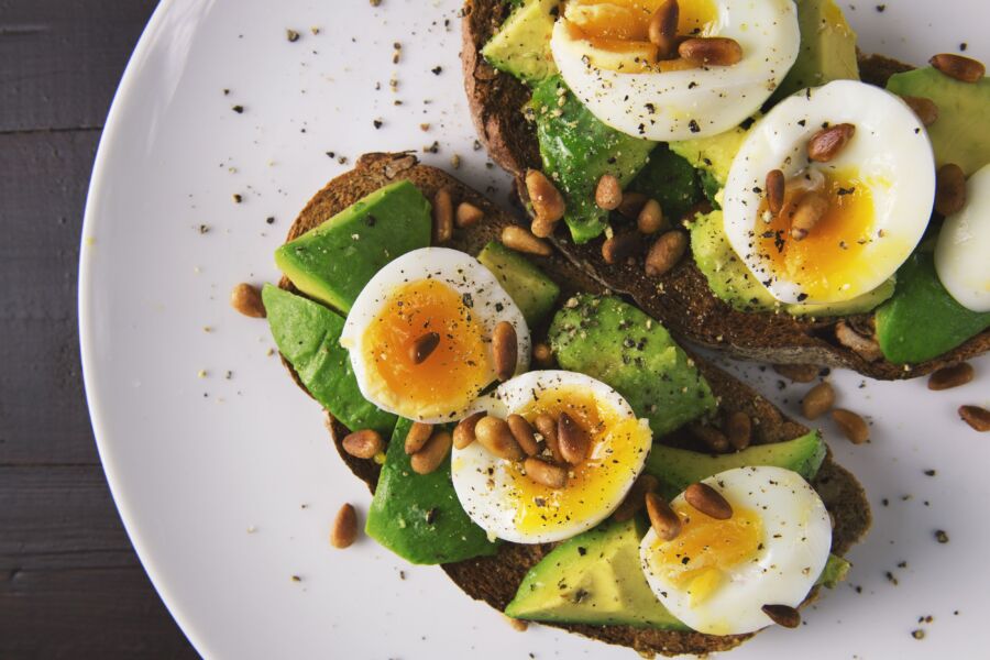 Deliciosas tostadas de aguacate cubiertas con huevos cocidos y piñones en un plato blanco.