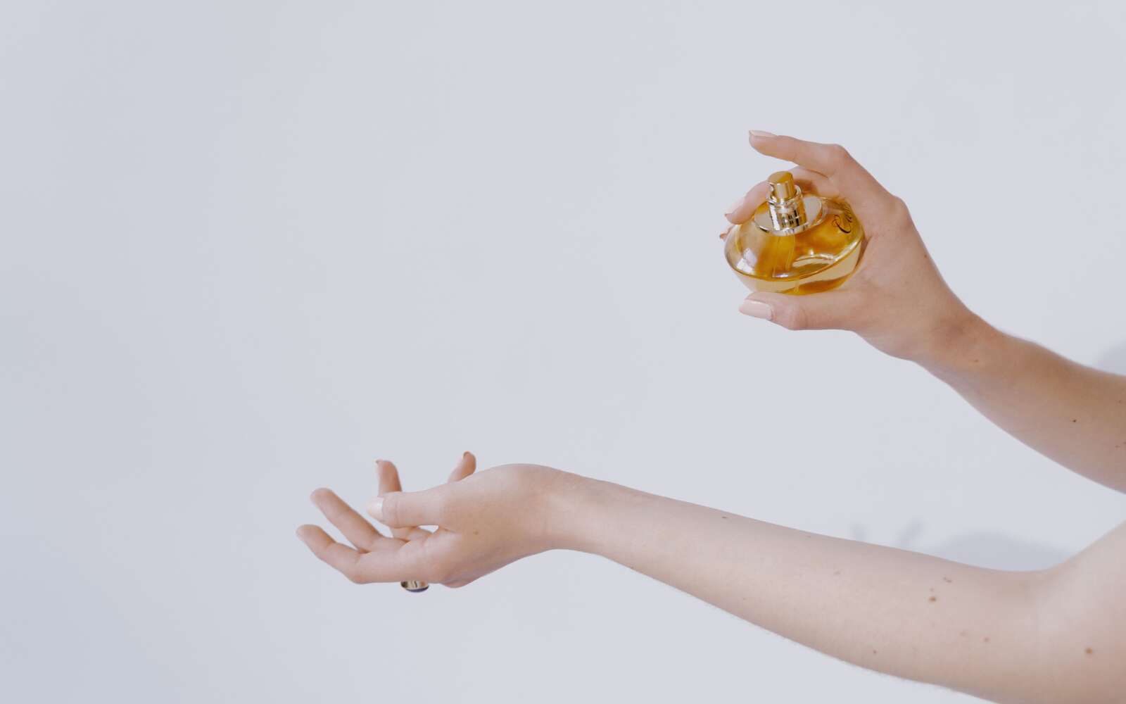 Primer plano de manos elegantes rociando perfume, mostrando belleza y lujo sobre un fondo blanco.