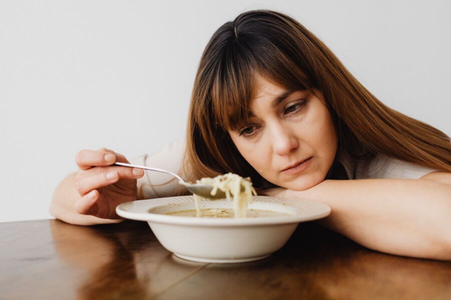 Una mujer sentada en una mesa mirando pensativamente un tazón de sopa de fideos, evocando un sentido de contemplación.