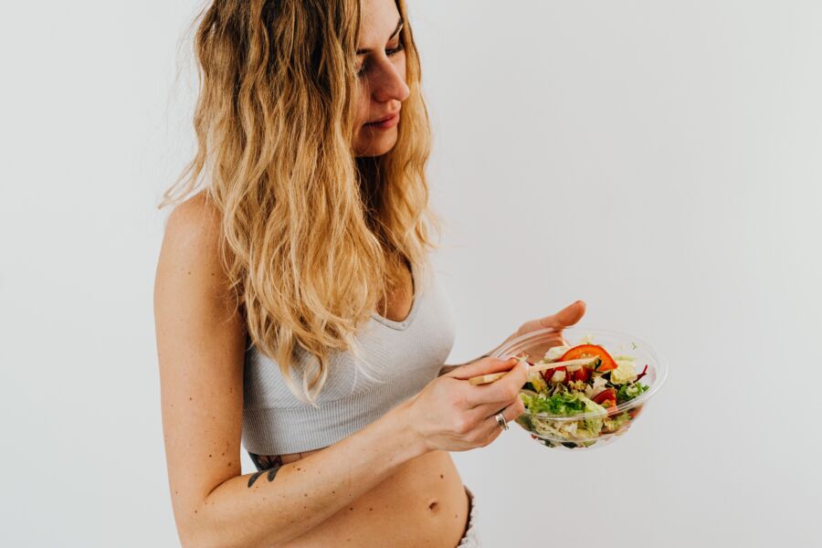 Una mujer caucásica en un sujetador deportivo disfrutando de una ensalada fresca, que encarna una alimentación y un estilo de vida saludables.