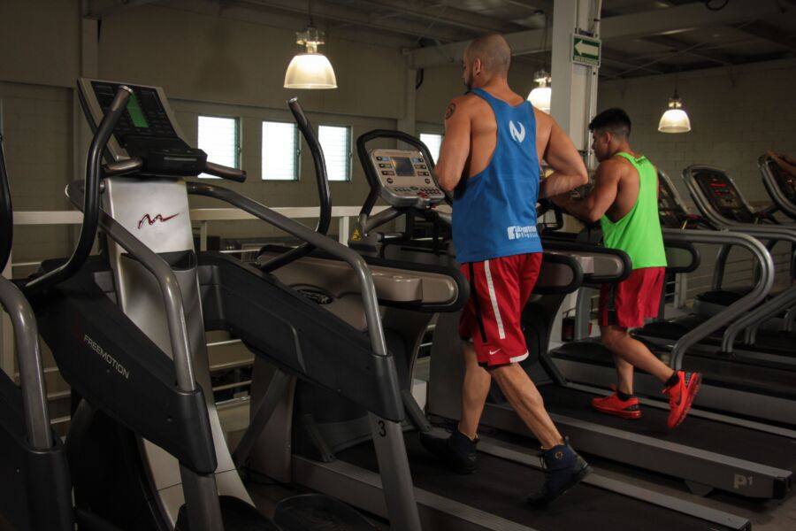Dos hombres corriendo en cintas de correr en un gimnasio moderno, promoviendo el fitness y la salud.