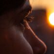 Un primer plano cautivador del ojo de una persona con una puesta de sol vibrante en el fondo, creando un ambiente cálido e introspectivo.