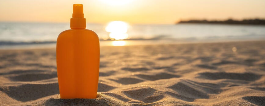 Botella de protector solar en una playa de arena durante la puesta de sol