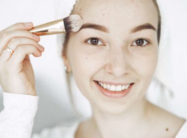 Retrato de una joven sonriente aplicando maquillaje con un pincel en interiores.