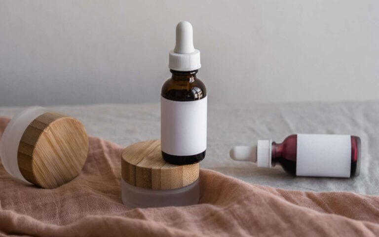 Configuración minimalista de botellas para el cuidado de la piel con tapas de bambú sobre una superficie textil.