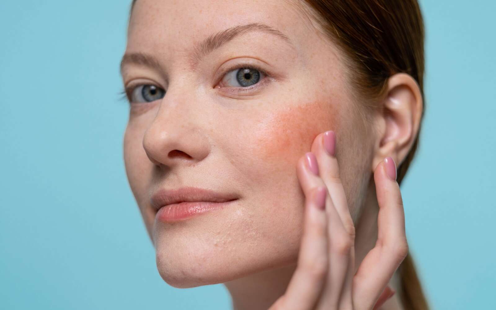 Mujer aplicando rubor en su rostro, destacando la piel sana y la belleza en un entorno de estudio.